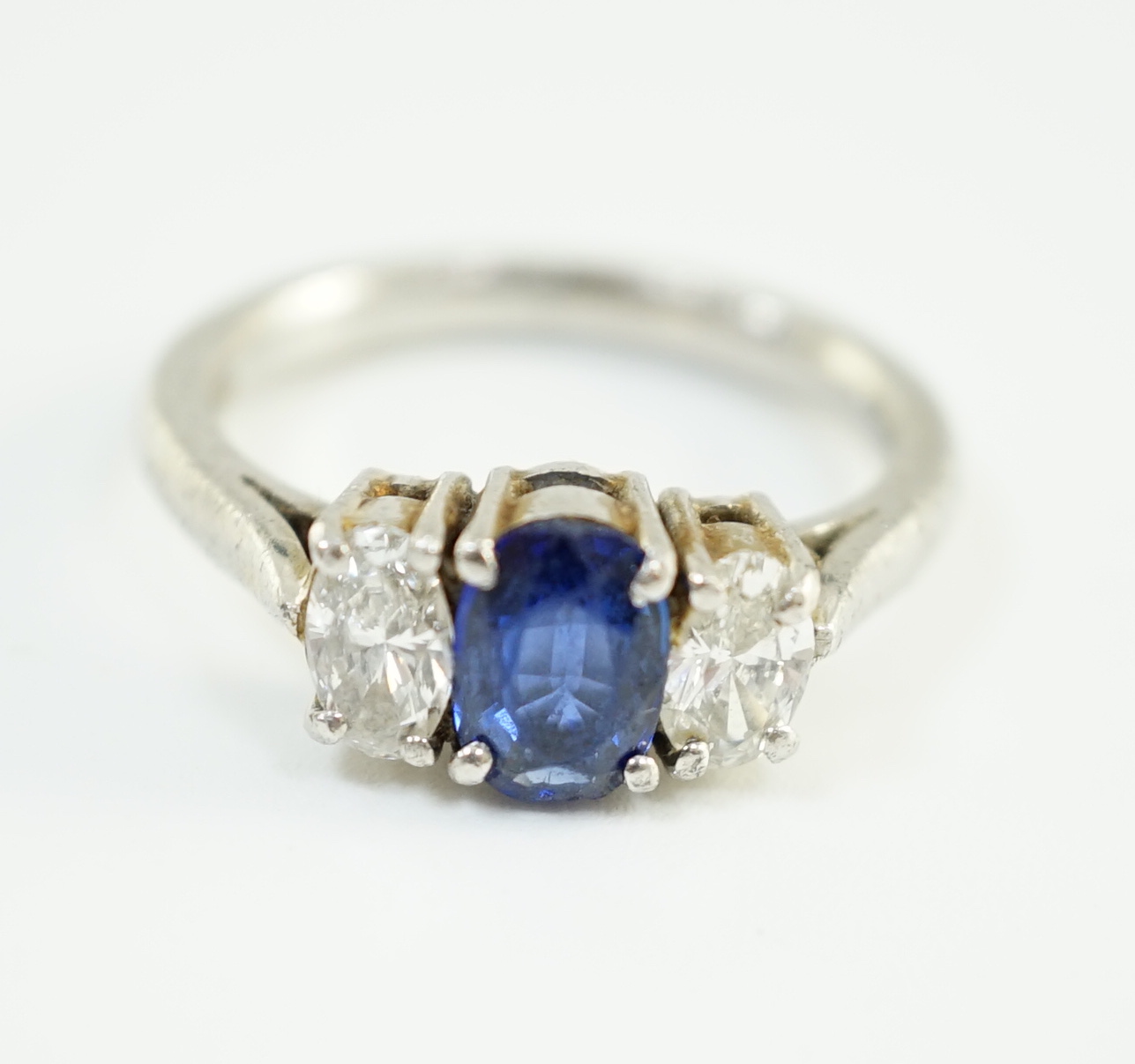 A modern platinum, singe stone oval cut sapphire and two stone oval cut diamond set ring